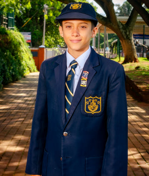 Young boy in a formal school uniform standing outdoors on a sunny day.